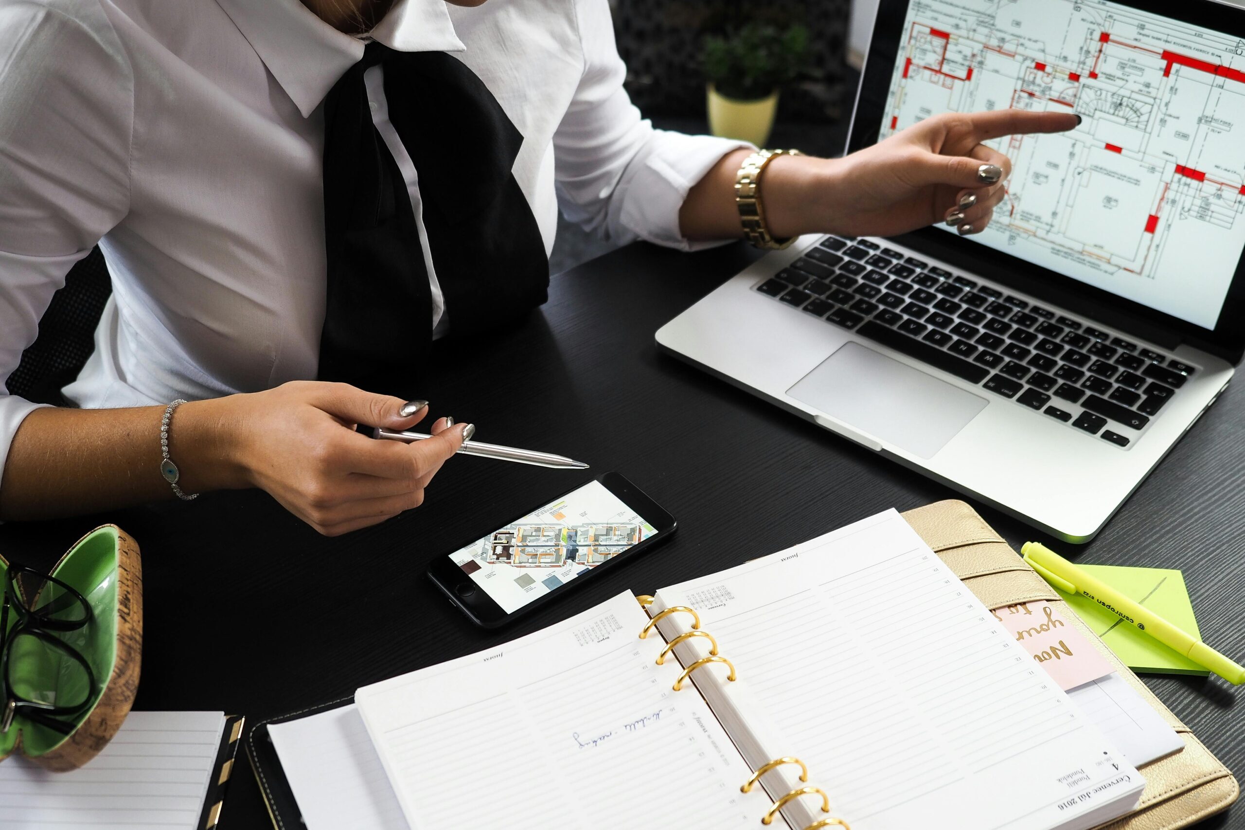 A business professional working on real estate project plans using multiple devices in an office setting.