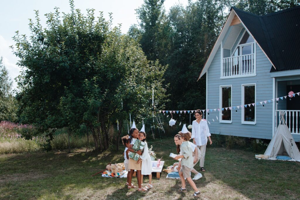 Children playing at a summer outdoor party beside a cozy house with nature backdrop.