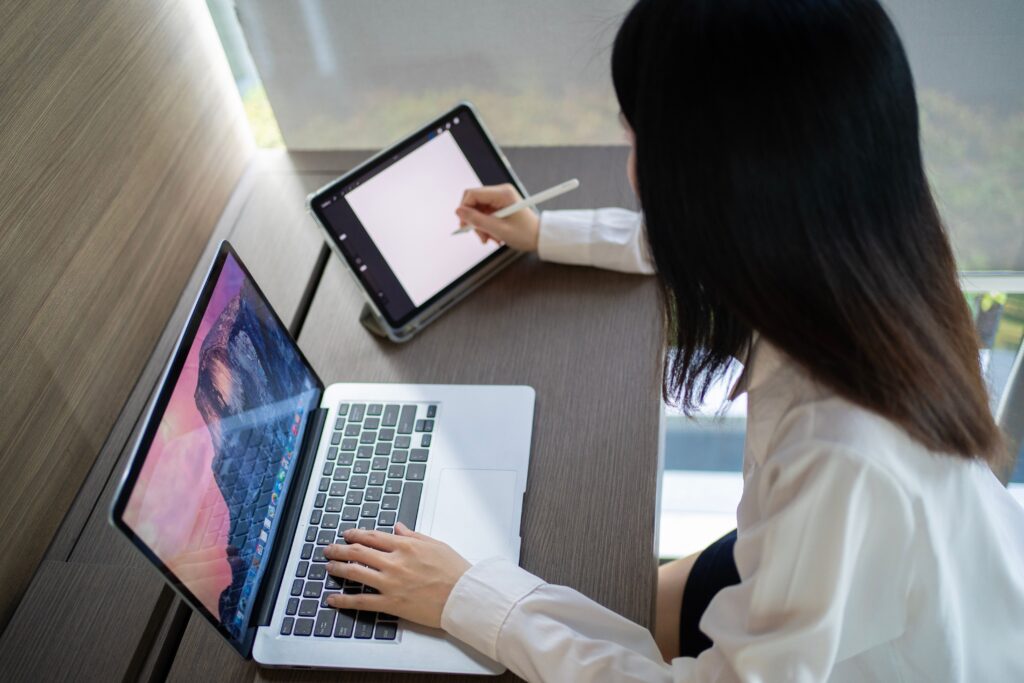 Asian woman multitasking with laptop and tablet in a modern home office in Bangkok.